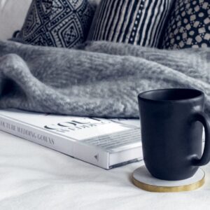 A cozy interior scene featuring a black mug, a book, and patterned pillows on a soft couch.